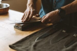 Couteau de cuisine bien aiguisé posé sur une planche en bois, entouré d’outils comme une pierre à aiguiser pour illustrer un guide pour aiguiser un couteau