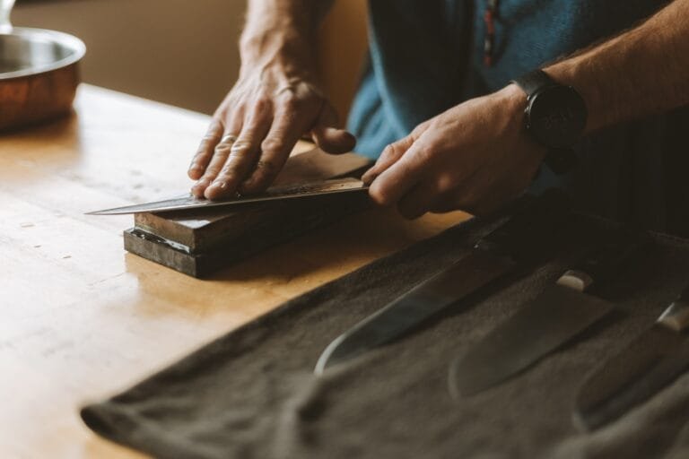 Couteau de cuisine bien aiguisé posé sur une planche en bois, entouré d’outils comme une pierre à aiguiser pour illustrer un guide pour aiguiser un couteau
