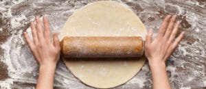 Préparation en cuisine pour foncer un moule à tarte avec une pâte étalée, un rouleau à pâtisserie et de la farine