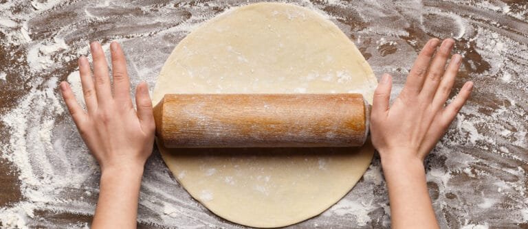 Préparation en cuisine pour foncer un moule à tarte avec une pâte étalée, un rouleau à pâtisserie et de la farine