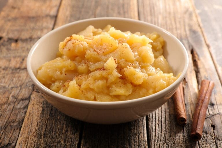 Bol de compote de pommes maison préparé rapidement avec une texture fondante, servi dans un plat en céramique blanche de la canelle.