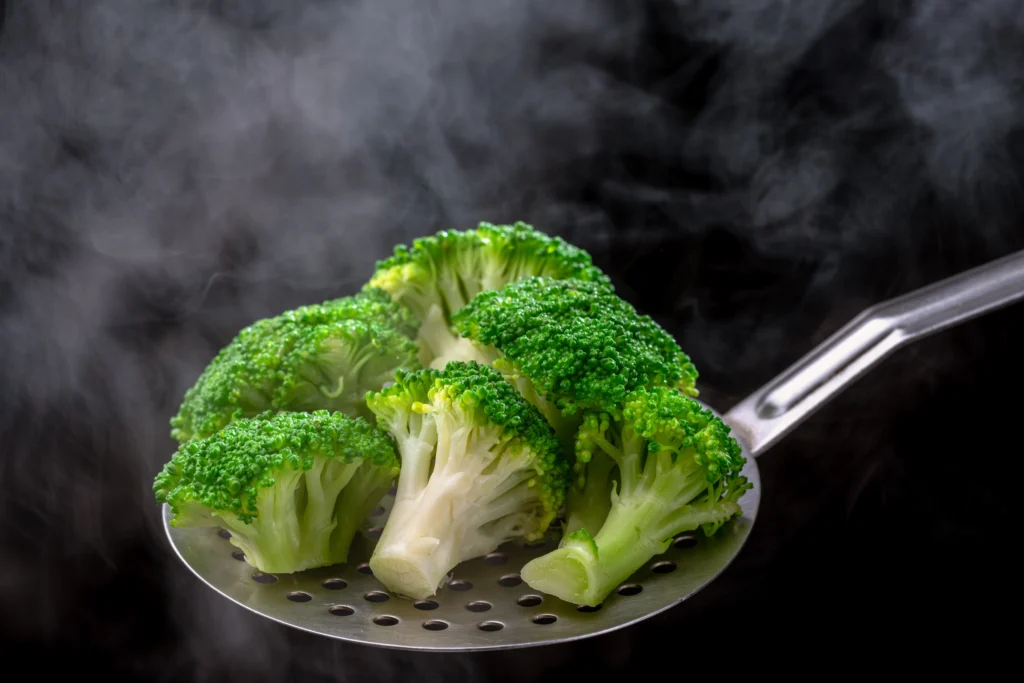 Brocolis verts cuits à la vapeur dans un écumoir, conservant leur couleur éclatante et leur texture croquante.