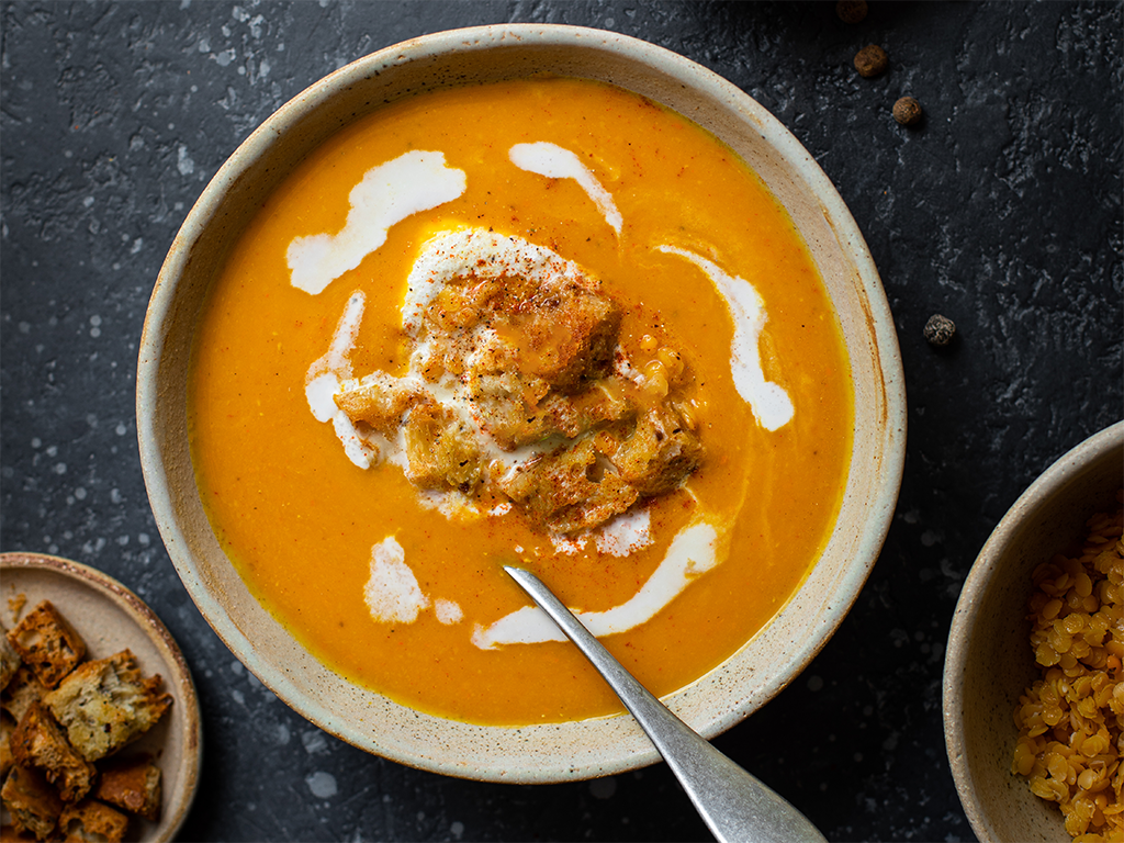Soupe veloutée au potiron, lentilles corail et lait de coco, servie chaude dans un bol avec une touche de coriandre