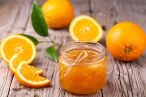 Pot de confiture d’orange fait maison entouré de tranches d’orange fraîches sur une table en bois rustique.
