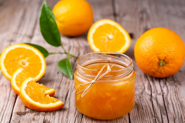 Pot de confiture d’orange fait maison entouré de tranches d’orange fraîches sur une table en bois rustique.