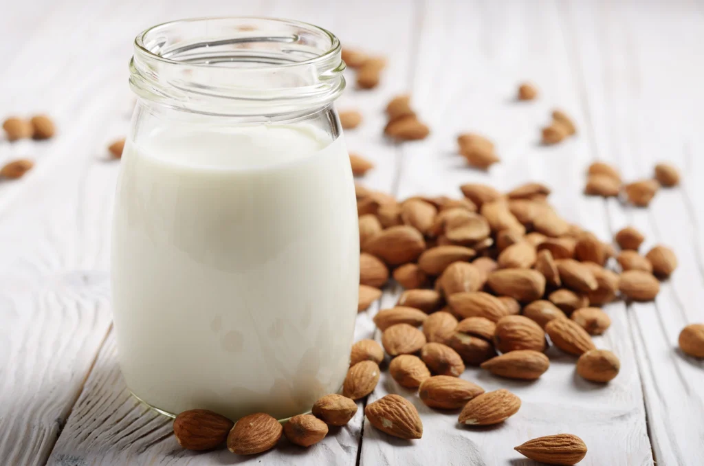 Bocal de crème d’amande posé sur une table en bois clair, entouré d’amandes – alternative végétale sans lactose à la crème fraîche
