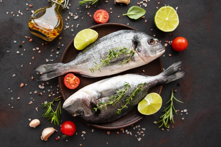 Deux dorades fraîches sur assiette avec herbes aromatiques, citron vert, tomates cerises et épices, prêtes à être cuisinées