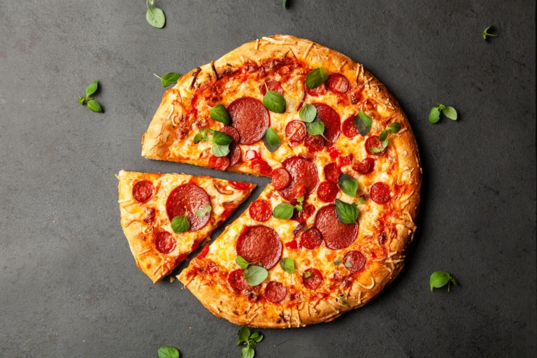 Pizza maison au pepperoni, fromage fondu et feuilles de basilic, servie sur fond sombre avec une part découpée