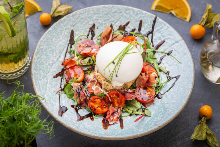 Salade fraîche avec burrata, tomates cerises, jambon cru et roquette, nappée de vinaigre balsamique sur une assiette en céramique bleue