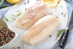 Deux dos de cabillaud crus posés sur une planche avec herbes, poivre et citron