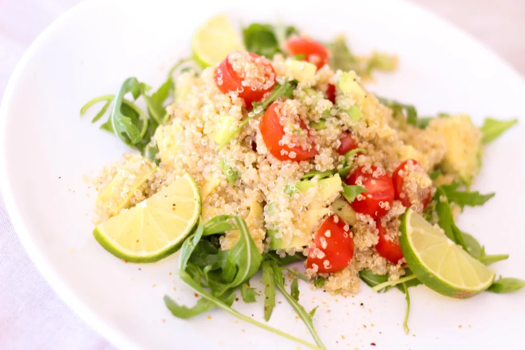 Photo d’une assiette de salade de quinoa colorée avec avocat, citron vert, tomates cerises et roquette