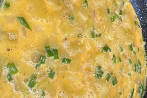 Mélange d’œufs, pommes de terre en dés et ciboulette en cuisson pour une tortilla espagnole maison