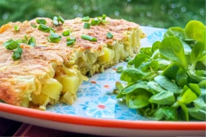 Part de tortilla espagnole maison montrant les pommes de terre fondantes avec ciboulette et salade de mâche
