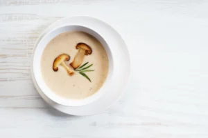 Bol de velouté de champignons crémeux décoré de champignons poêlés et romarin