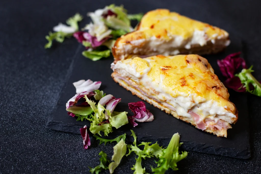 Croque-monsieur classique au four avec béchamel et salade verte sur ardoise noire