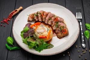 Assiette gastronomique de magret de canard rosé nappé de sauce à l’orange, pomme de terre au bleu, carottes glacées et salade de jeunes pousses