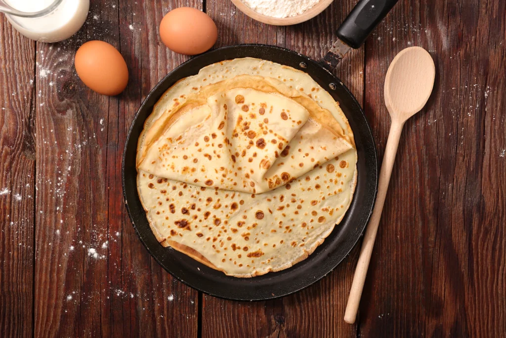 Crêpes dorées dans une poêle en fonte sur planche rustique – recette de pâte à crêpe maison facile