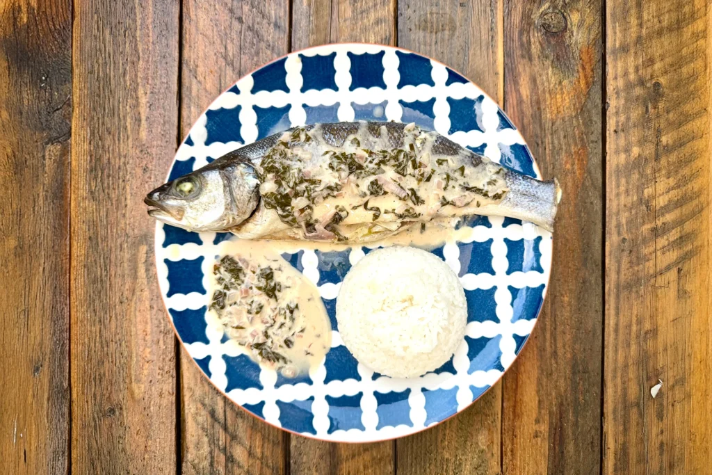 Assiette bleue avec bar entier rôti, sauce à l’oseille, riz, vue du dessus sur une table en bois.