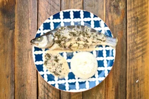 Assiette bleue avec bar entier rôti, sauce à l’oseille, riz, vue du dessus sur une table en bois.