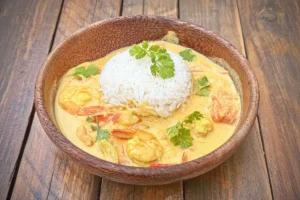 Bol en bois contenant plat de crevette curry coco avec riz et coriandre fraîche