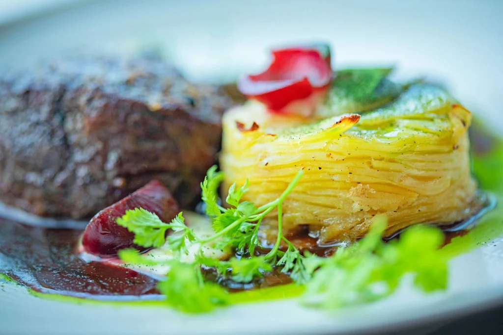 Millefeuille de pommes de terre doré au four servi avec une sauce et des herbes fraîches