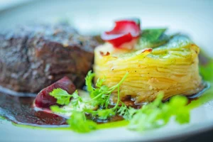 Millefeuille de pommes de terre doré au four servi avec une sauce et des herbes fraîches