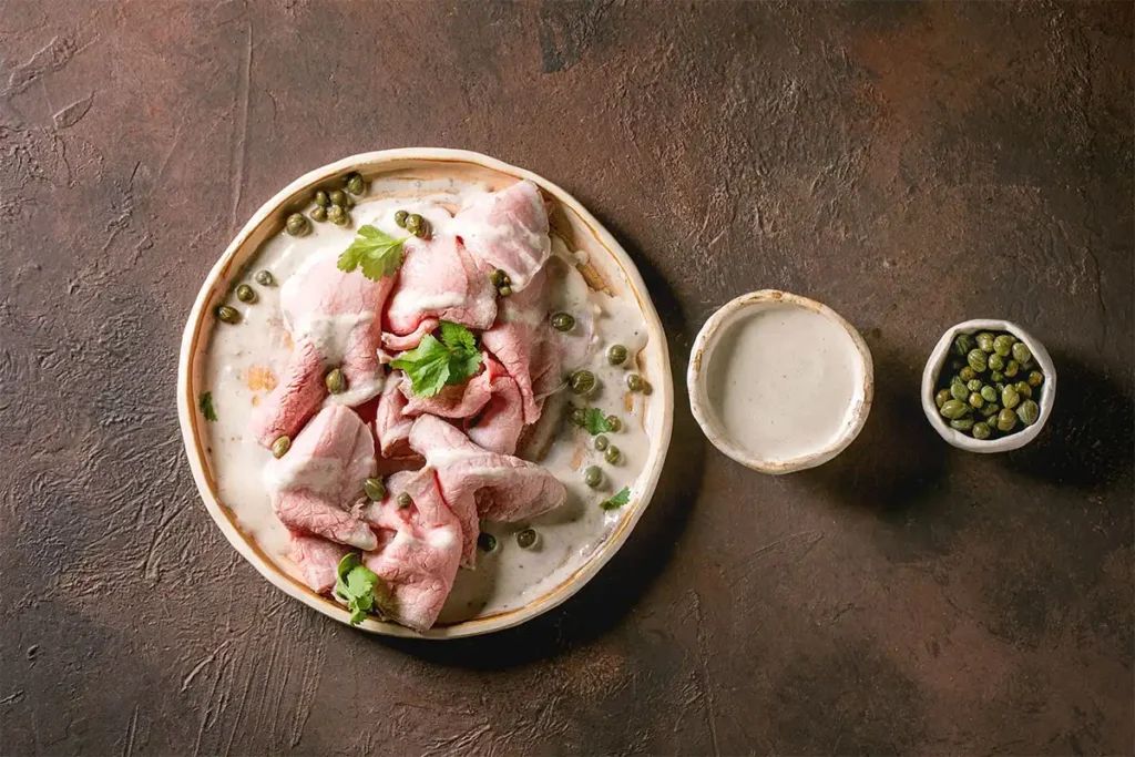 Tranches de veau nappées de sauce tonnato avec câpres et persil sur assiette