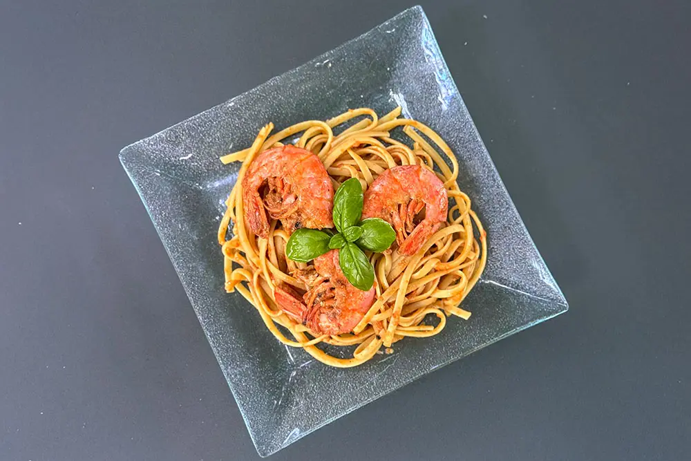 Assiette de gambas à la catalane sur linguine, nappées de sauce tomate et décorées de basilic