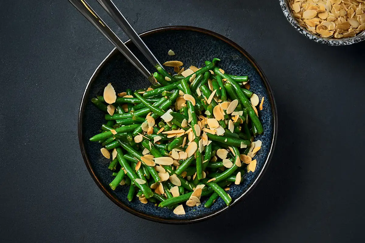 Haricots verts amandine servis dans une assiette bleue avec amandes grillées