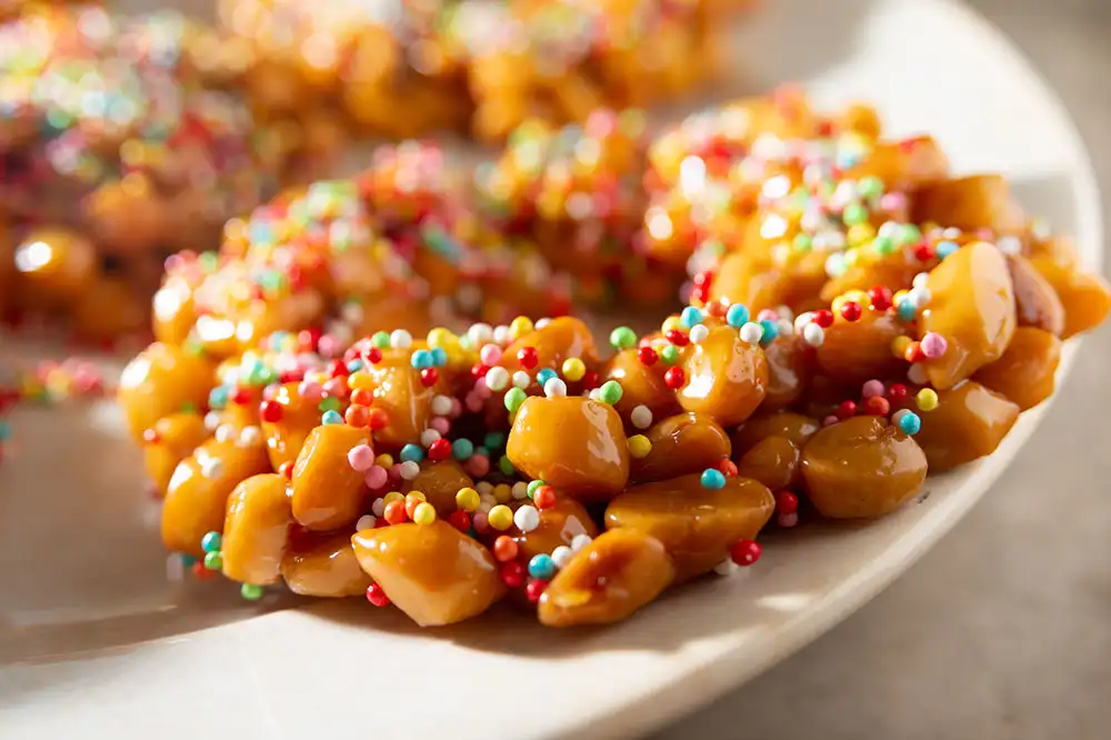 Struffoli napolitains, petites boules de pâte dorées enrobées de miel et décorées de perles colorées, dessert traditionnel de Noël à Naples.