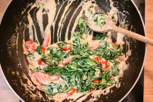 Préparation de la sauce crémeuse aux épinards et tomates cerises dans une poêle, pour le saumon à la toscane