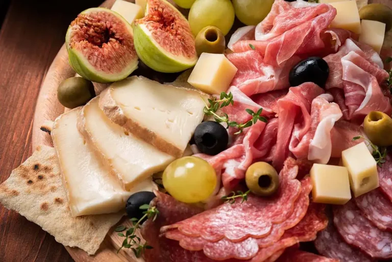 Planche apéritive artisanale garnie de charcuteries fines, fromages, figues fraîches et raisins sur une table en bois.