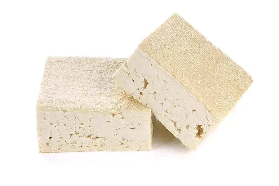 Deux blocs de tofu ferme nature, dont un coupé, montrant une texture poreuse.