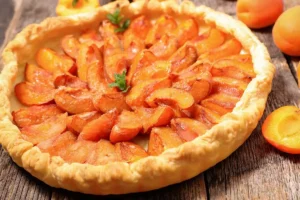 Tarte aux abricots frais et fondants selon la recette traditionnelle de grand-mère, avec une pâte feuilletée pur beurre dorée et croustillante sur un fond en bois rustique.