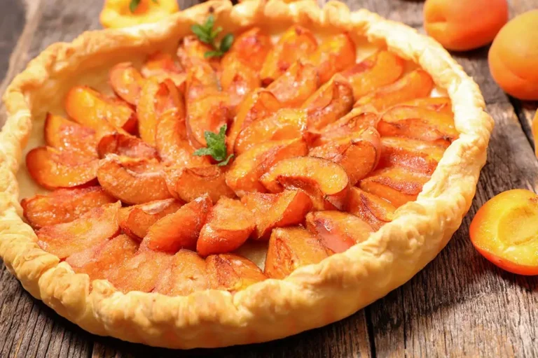 Tarte aux abricots frais et fondants selon la recette traditionnelle de grand-mère, avec une pâte feuilletée pur beurre dorée et croustillante sur un fond en bois rustique.