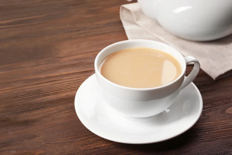 Une tasse de thé anglais noir avec un nuage de lait, posée sur une table en bois à côté d'une théière.