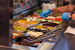 Préparation d'une salade avec des ingrédients frais stockés dans les bacs gastronormes d'une saladette réfrigérée.