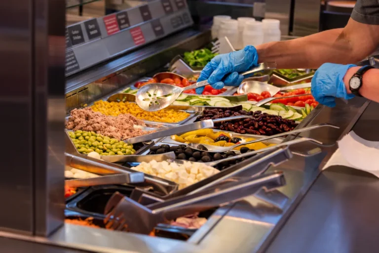 Préparation d'une salade avec des ingrédients frais stockés dans les bacs gastronormes d'une saladette réfrigérée.