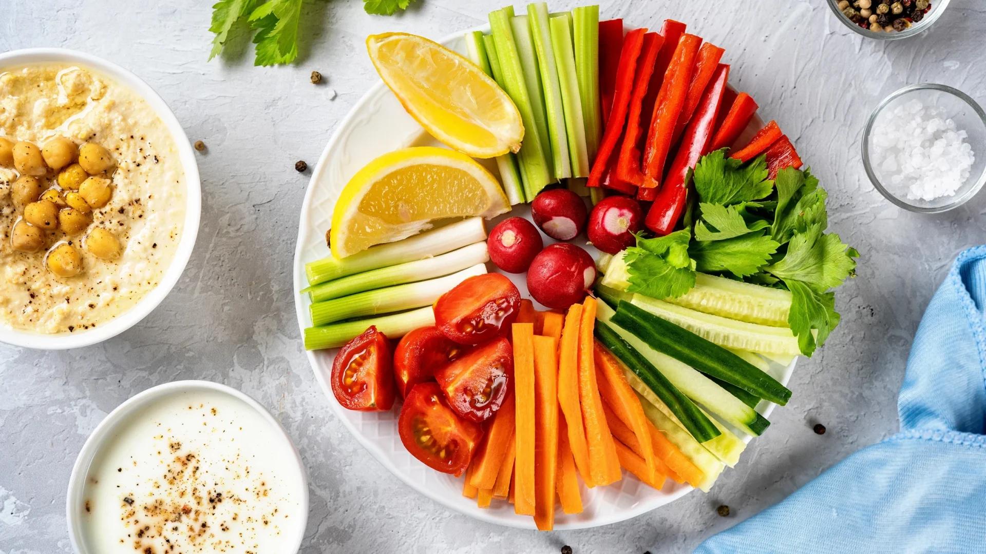 Assiette apéritive colorée avec bâtonnets de légumes frais, citron, houmous et sauce au yaourt sur fond clair