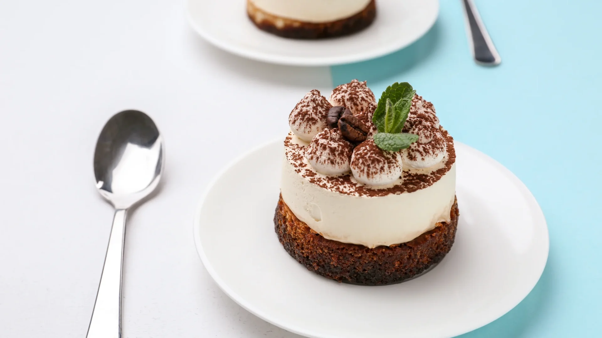 Cheesecake individuel au café, décoré de crème, cacao et feuilles de menthe, sur assiette blanche avec cuillère