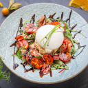 Salade fraîche avec burrata, tomates cerises, jambon cru et roquette, nappée de vinaigre balsamique sur une assiette en céramique bleue